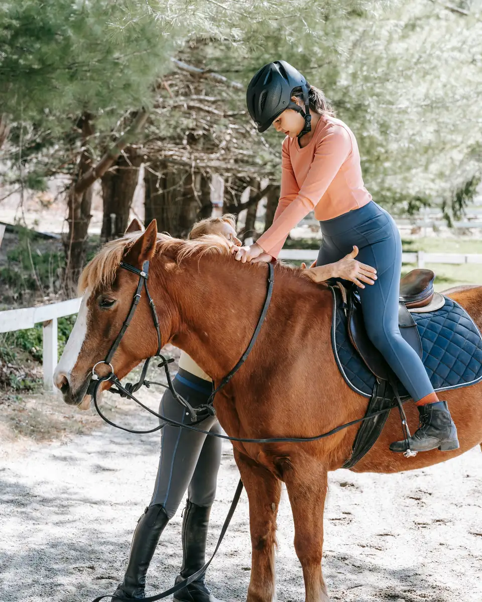 A coach on foot steadies a rider on a chestnut horse during a lesson.